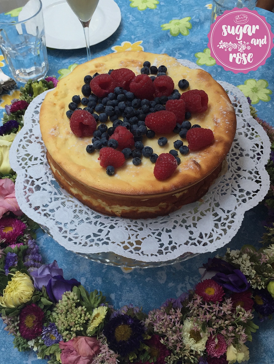 Runder Topfenkuchen ohne Boden, bedeckt mit Heidelbeeren und Himbeeren und Rosensirup