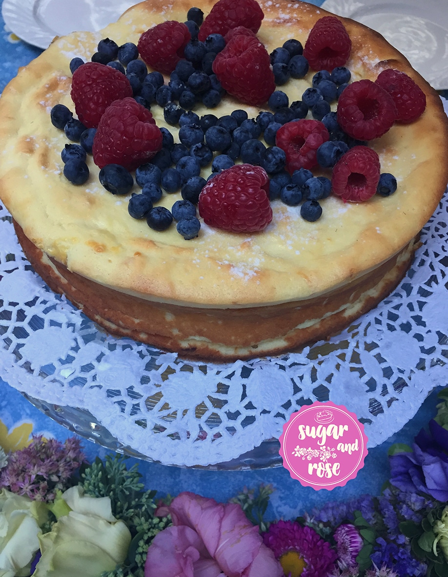 Runder Topfenkuchen ohne Boden, bedeckt mit Heidelbeeren und Himbeeren und Rosensirup