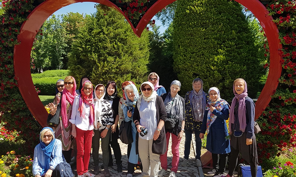 Botanisch Interessierte Reisegruppe "Persien zur Rosenblüte" vor einem roten Herz in einem Garten
