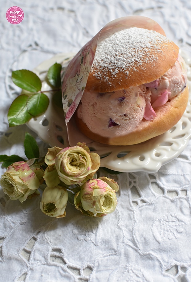 Eisburger (Brioche con Gelato) in Papiertüte mit Rosenmotiv, gefüllt mit Roseneiskugeln, daneben kleine grüne Rosen