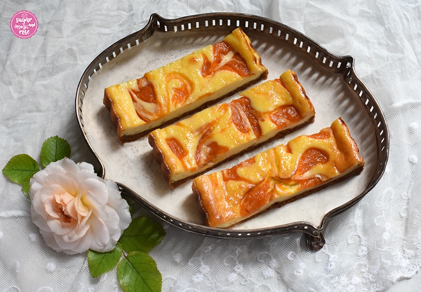 Drei Stück Marillen-Tarte Schnitten auf einem silbernen Jugendstiltablet, dekoriert mit einer milchigweißen Rosenblüte 