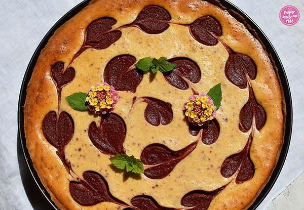 Ungezuckerte, gebackene Käsetarte mit Fruchtmus, dekoriert mit Minze und kleinen rosa Blütendolden