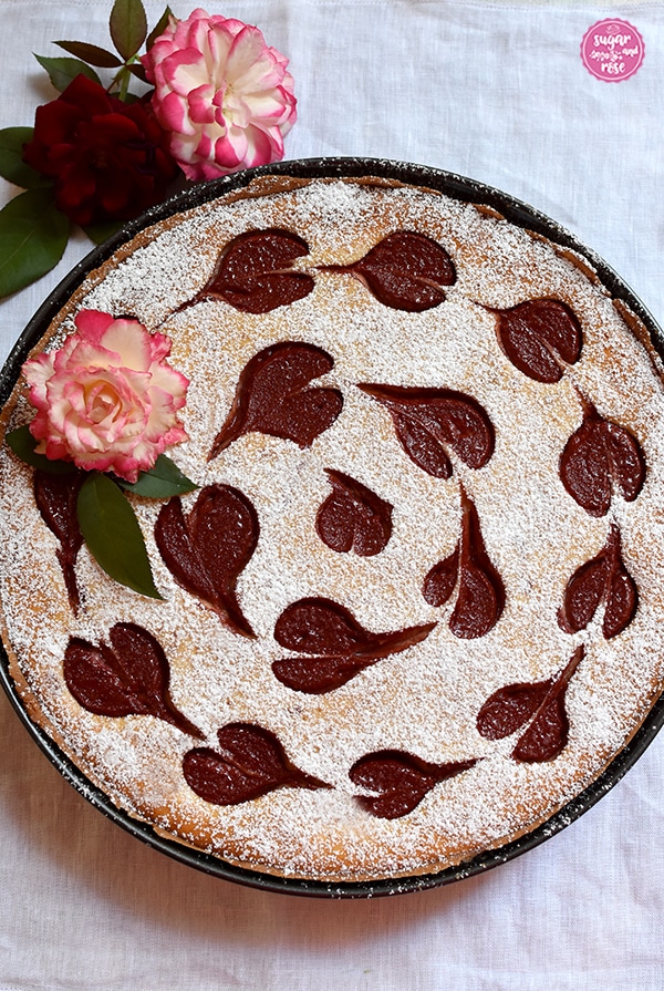 Herzerl-Ricotta-Tarte mit Zwetschkenmus in einer runden Tarteform, dekoriert mit rotrandigen Rosen