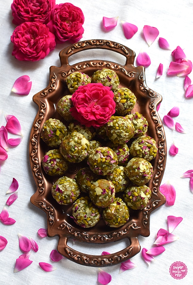 Kupfertablett mit Henkeln, darauf ein Menge Rosen-Safran-Energiekugeln, obenauf eine Rosenblüte, rund um das Tablett einzelne Rosenpetalen der Rose de Resht