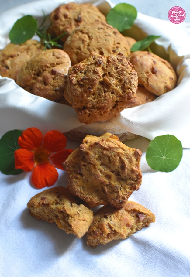 Kürbis-Speckweckerl im Brotkörbchen, davor angebrochene Weckerl und eine orangefarbene Kapuzinerkresseblüte