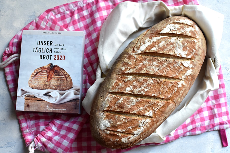 Brotkörbchen mit einem Bauernbrotstrietzel, auf einem rosa-weiß karierten Brotsack, daneben der Tagesabreisskalender "Unser täglich Brot. Mit Laib und Seele durch 2020"