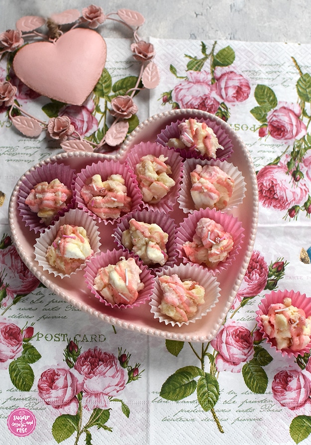 Rocky Road Konfekt in rosa und weißen Pralinenförmchen in einer rosa Keramikherzschale auf einer Serviette mit Rosenmotiven