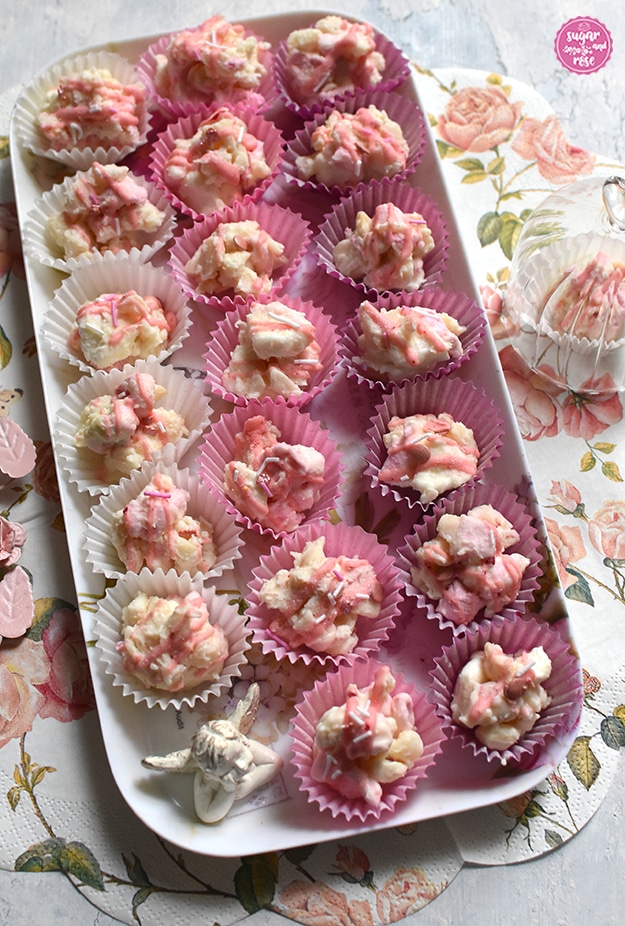 Rocky Road Konfekt in rosa und weißen Pralinenförmchen auf einem länglichen Tablett in drei Reihen aufgelegt, links in weißen, mittig in hellrosa, rechts in zyklamfarbigen Papierkonfektformen