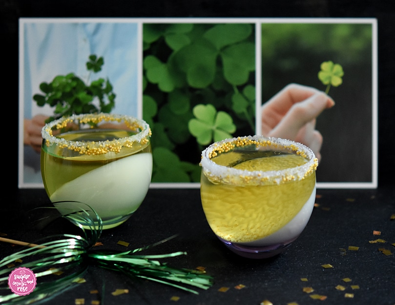 Zwei bauchige kleine Cocktailgläser mit Sektjelly, davor Goldflitter, dahinter eine Karte mit Glücksklee