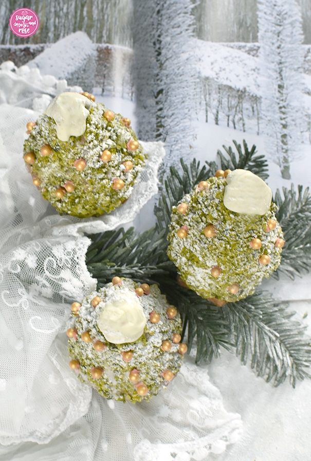 Drei süße Weihnachtsbäume zum Vernaschen mit Goldzuckerperlendeko auf einem beschneiten Tannenzweig, dahinter eine Zeitschrift mit verschneiter Winterlandschaft