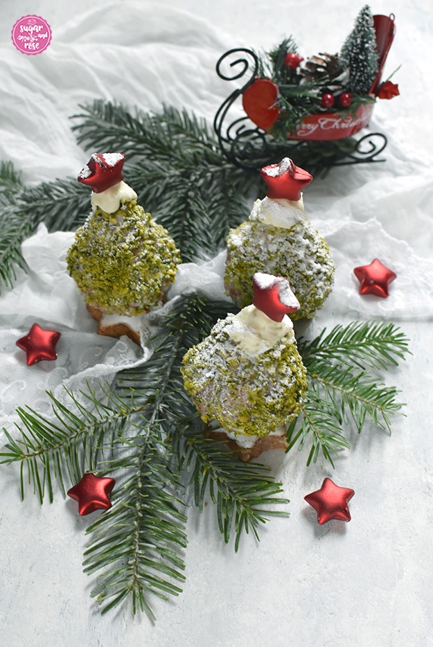 Drei Weihnachstbäume zum Vernaschen auf angezuckerten Tannenzweigen, dahinter ein roter Dekoweihnachtsschlitten, vorne kleine rote Dekosterne