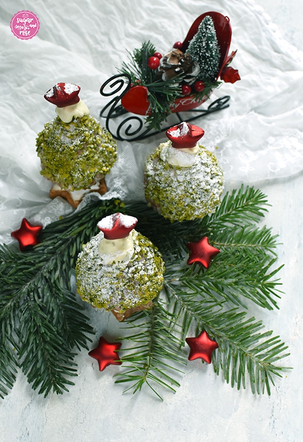 Drei Weihnachstbäume zum Vernaschen auf einem Tannenzweig, dahinter ein roter Dekoweihnachtsschlitten, vorne kleine rote Dekosterne