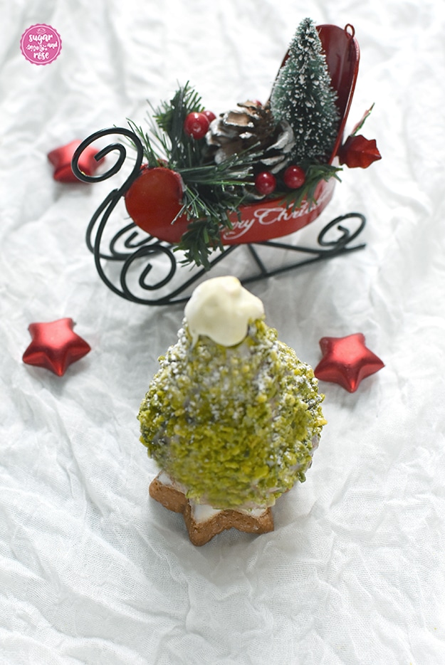 Ein süßer Weihnachtsbaum zum Vernaschen mit Pistazienkleid, auf einem Zimtstern stehend, an der Spitze weiße Kuvertüre, drei rote Dekosterne und der rote Dekometallschlitten mit der Aufschrift "Merry Christmas"
