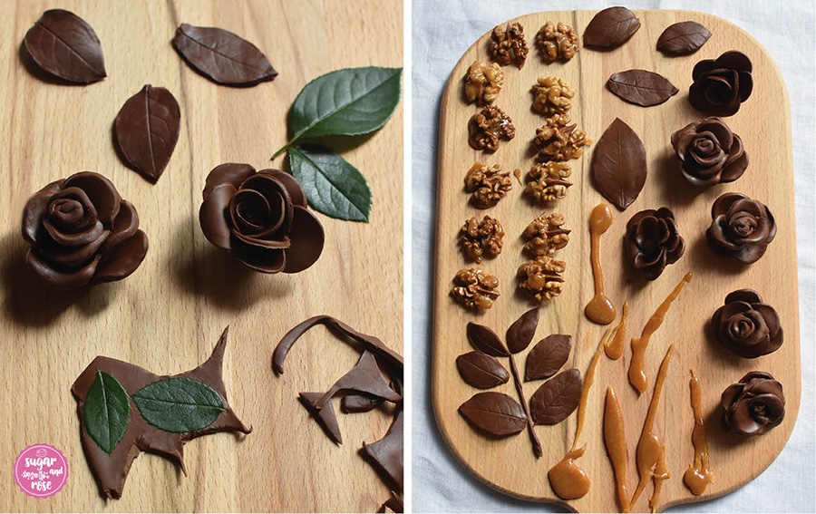 Links zwei fertige Schokoladerosen, Reste der Modellierschokolade und grüne Rosenblätter; rechts auf einem Holzbrett fertige Rosenblüten und Blätter aus Modellierschokolade sowie karamellisierte Walnusshälften