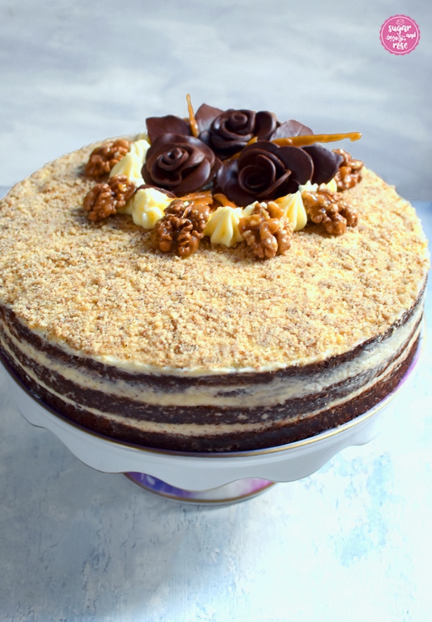 Walnusstorte mit karamellisierten Walnüssen auf einem Tortenteller mit Keramikfuss von der Seite, sodass man die drei Tortenböden und die Cremefüllung sieht