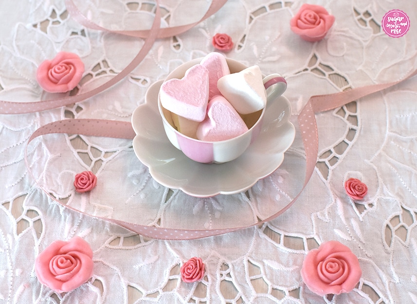 Augarten-Melone-Mokkatasse mit rosa Marshmallowherzen gefüllt auf weißem Lochstickerei-Tischset, dekoriert mit kleinen rosa Zuckerröschen und rosa Schleife