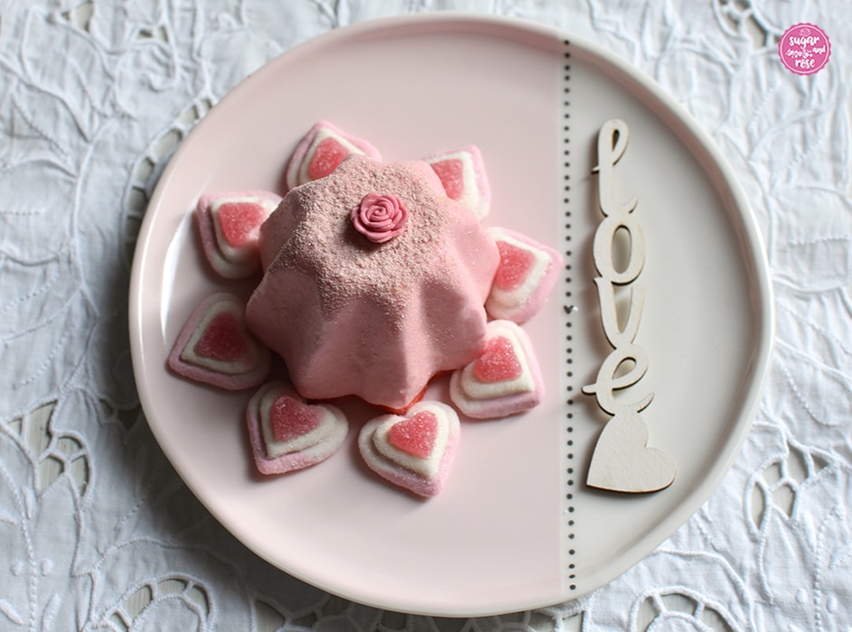Weiß-rosa Keramikteller, darauf ein rosa Joghurttörtchen in Sternform, rundum das Törtchen liegen acht rosa-weiße Marshmallowherzen.