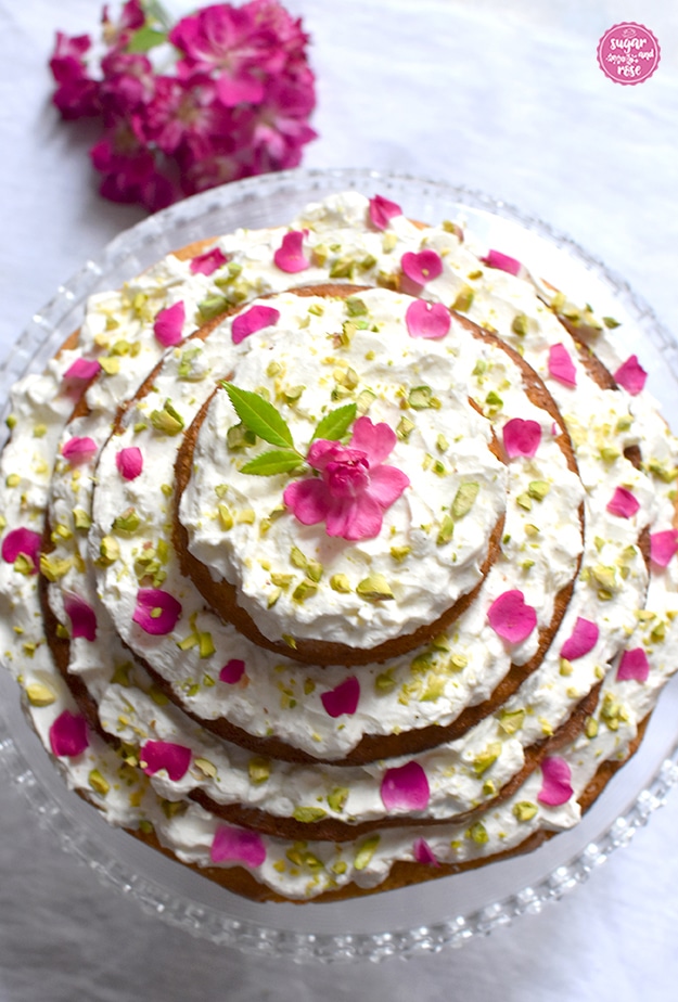 Karottenkuchen mit Frischkäsefrosting auf Glasetagere von oben, dahinter eine pinke Rosenblütendolde