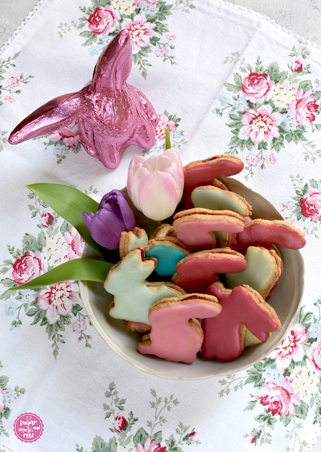 Osterhasen-Kekse in einer hellen Porzellanschale mit Tulpenblüte, dahinter ein pinkfarbener Schokoladenosterhase