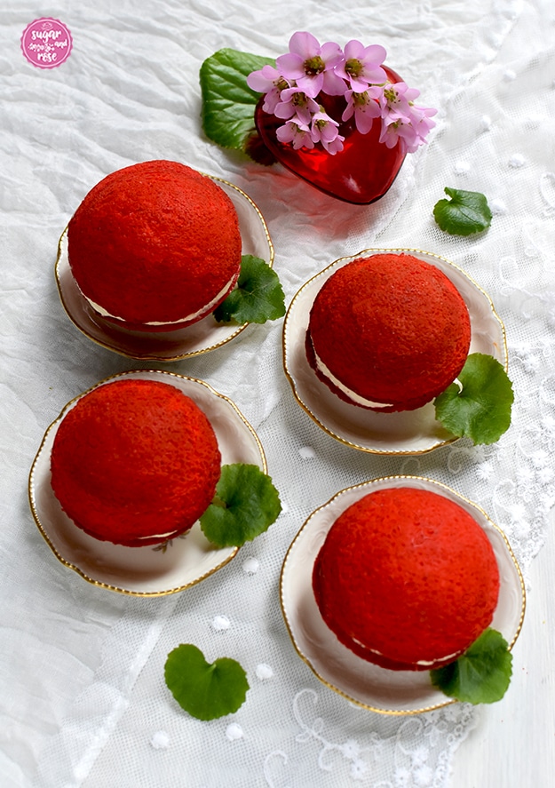 Oh-Wow-Whoopie in rot-weiß-rot: vier Stück auf kleinen Tellerchen, daneben jeweils grüne Blätter, dahinter ein rotes Glasherz mit rosa Steinbrech-Blüten