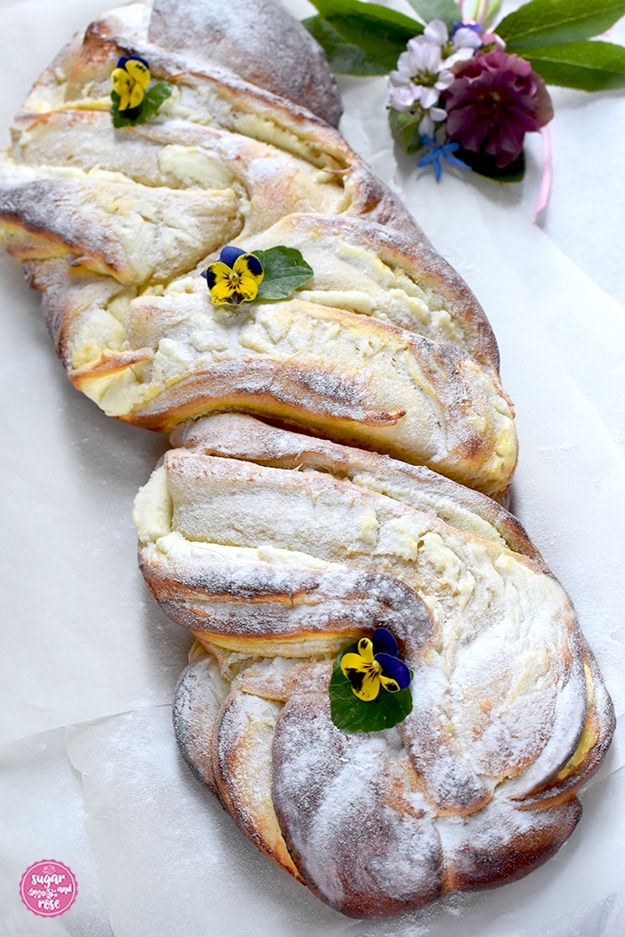 Topfen-Brioche auf Butterbrotpapier, mit Puderzucker und kleinen violett-gelben Violen dekoriert