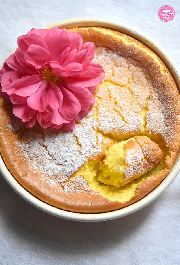 Grießauflauf in gelber Riess-Emailpfanne mit einer pinkfarbenen Rosenblüte dekoriert. Ein Stück vom Auflauf wurde bereits herausgestochen. Man sieht den safrangelben Auflauf innen.