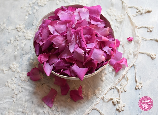 Eine weiße Keramikschale mit pinken Rosenblüten auf einem Vintagetuch mit aufgestickten Blüten