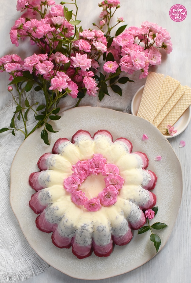 Eisgugelhupf von oben fotografiert, im Hintergrund mehrer Zweige mit rosa Röschen und ein kleiner weißer Teller mit Eiswaffeln.