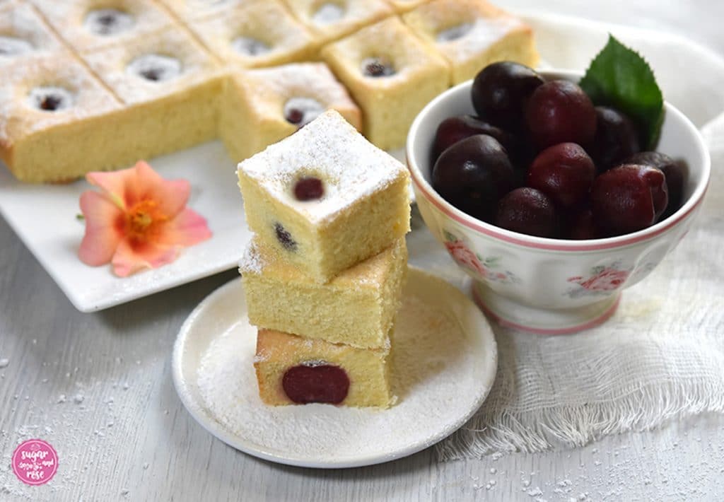 Rührteigkuchen mit Kirschen in Würfel geschnitten und teils übereinander gestapelt, daneben eine Schale mit Kirschen