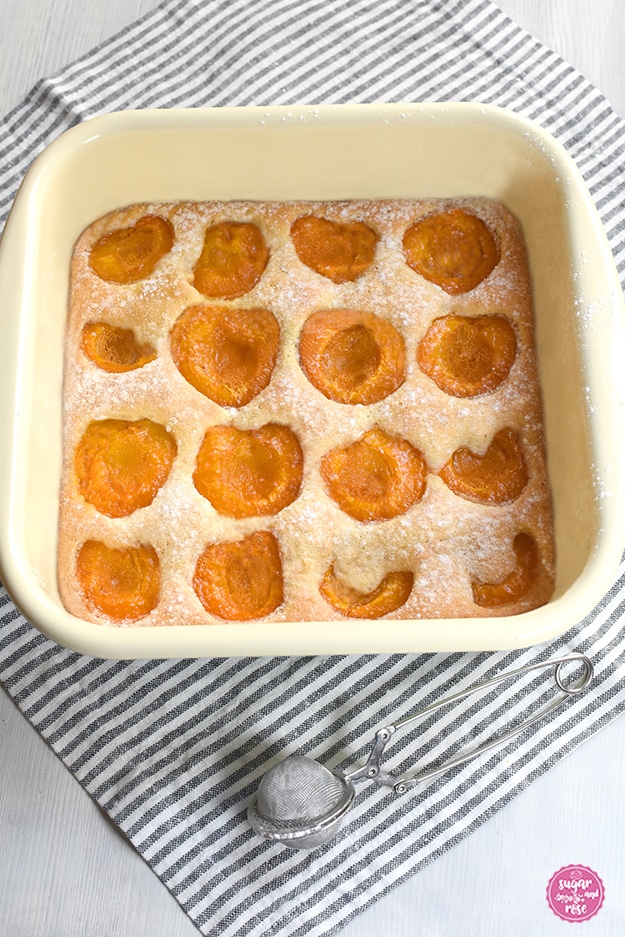 Obstkuchen mit Marillen in einer quadratischen Emailpfanne auf grau-weiß gestreifter Leinenserviette, davor ein Zuckerstreuer