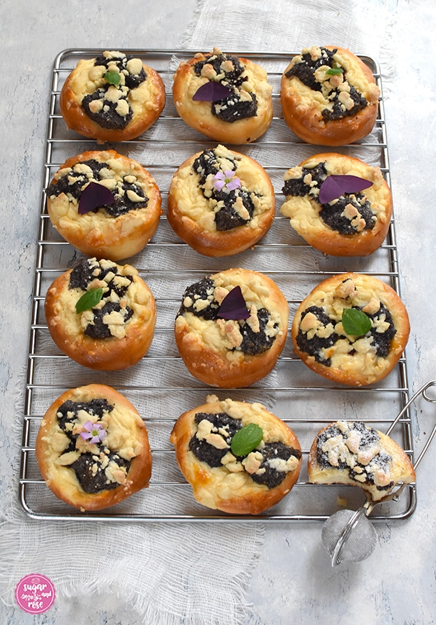 Eine der zwölf Kolatschen am Gitter ist bereits angebissen, daneben ein Puderzuckerstreuer.