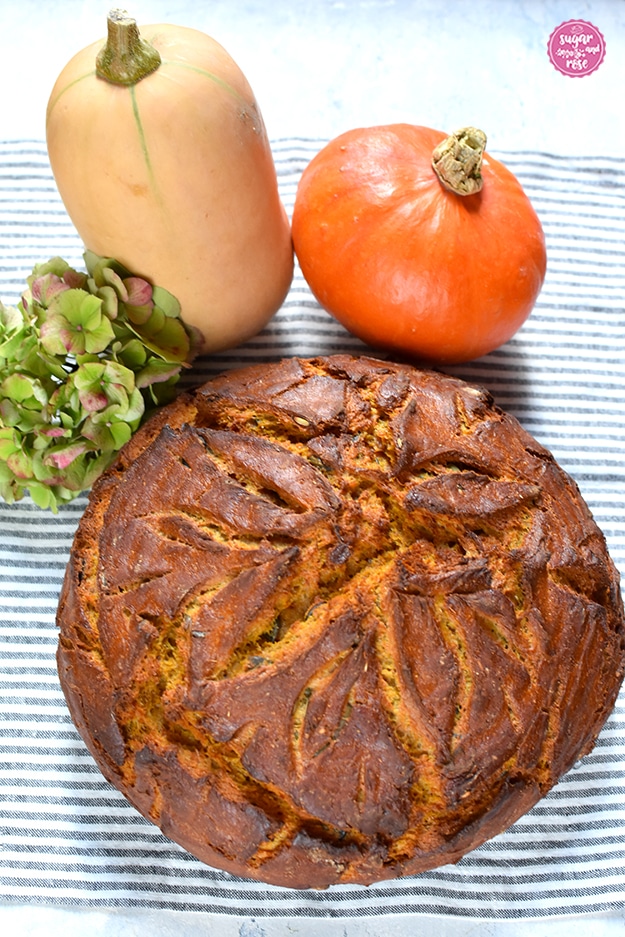 Ein Laib Kürbisbrot, dahinter ein Butternuss- und ein Hokkaidokürbis und eine grüne Hortensienblüte