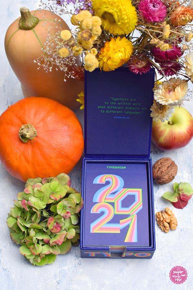 Typodarium-Tageskalender 2021 in blauer Kartonkasette, dekoriert mit zwei Kürbissen, Nüssen, Apfel und bunten Trockenblumen in herbstlichen Farben