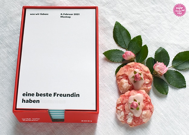 Notizkalender in der roten Box, zuoberst ist ein weißes Kalenderblatt vom 8. Februar 2021 zu sehen. In der linken oberen Ecke steht "Was wir lieben" und unten groß "eine beste Freundin haben". 