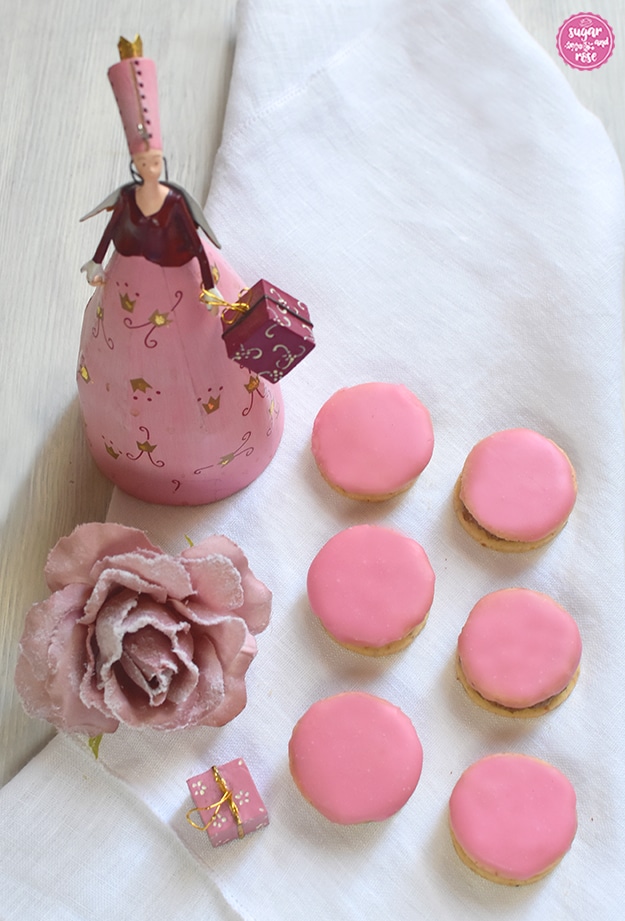 6 Punschtaler auf einer weißen Leinenserviette, daneben eine altrosa Kunstrosenblüte mit Raureif, dahinter eine rosa Blechfigur mir Engelsflügerl und einem Geschenkpaket in der Hand