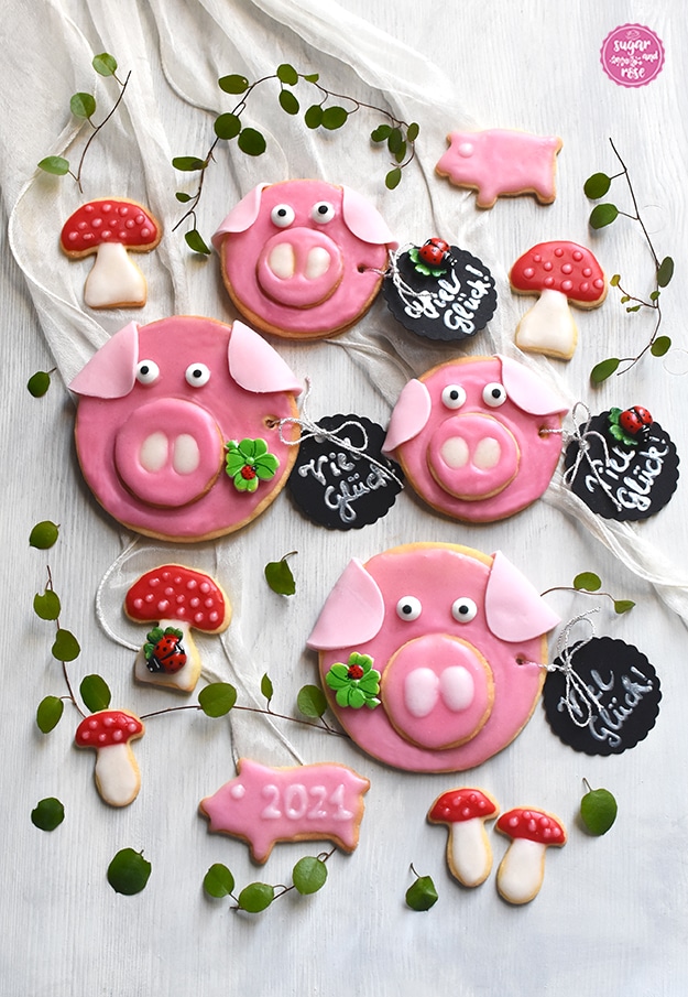 Große und kleine Glücksschweinchen und Glückspilze mit schwarzen runden Anhängern, auf denen "Viel Glück!" steht und Kleeblätter mit Marienkäferchen drauf.