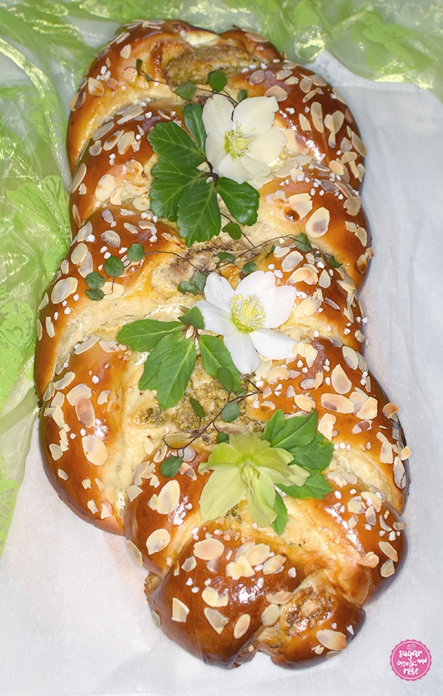 Briochestriezel (Hefezopf) mit Mandeln und Hagelzucker, dekoriert mit weißen Schneerosenblüten und grünen Blättern