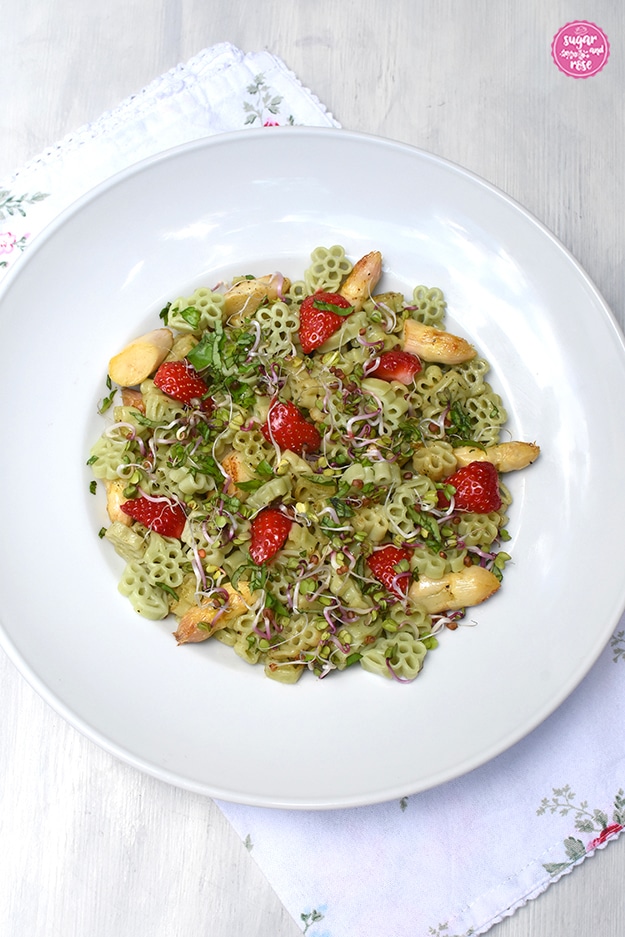 Tiefer weißer Pastateller mit hellgrünen Blütennudeln mit gebratenem weißem Spargel und Erdbeeren