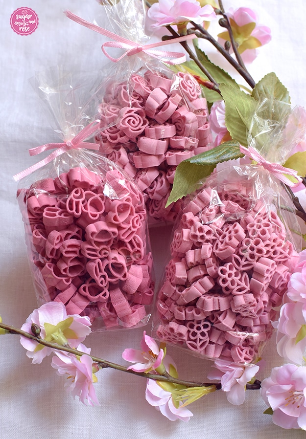 Drei Packungen hellrosa Blütennudeln in Häschen-, Blumen- und Rosenform in Cellophan mit rosa Schleife auf einem Kirschblütenzweig