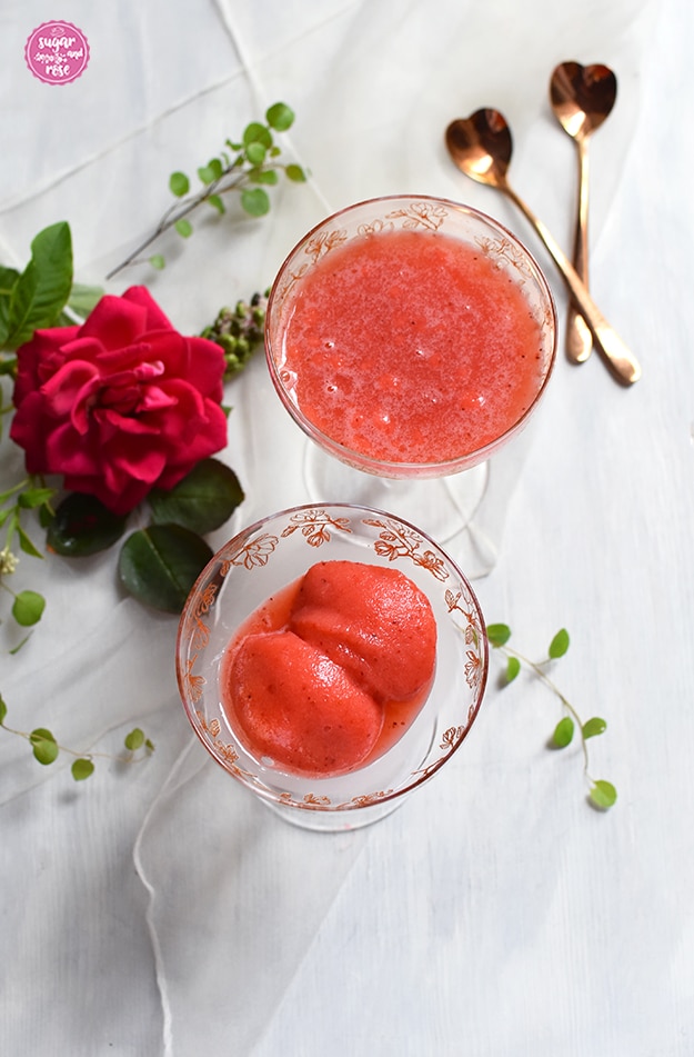 Zitrus-Erdbeersorbet mit zwei Löffelchen und einer pinken Rosenblüte
