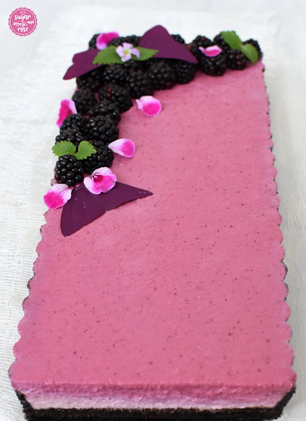 Angeschnittene Brombeertarte, man sieht den dunklen Oreo-Keksboden und die unterschiedlich farbigen Topfenschichten