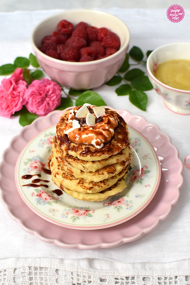 Fünf Panecakes übereinander gestapelt, daruaf Skyr und Dattelsirup und Kokoschips. Im Hintergrund Himbeeren und Apfelmus in Schalen