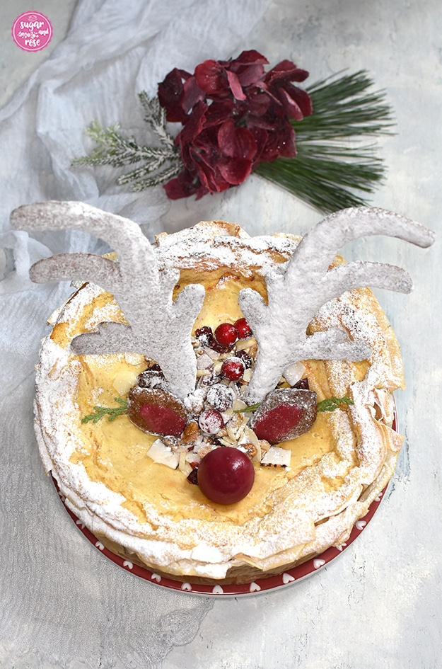 Spekulatius-Cheesecake mit weiß gezuckertem Rentiergeweih, zwei Lebkuchenohren und einer  roten Kugelnase, dahinter weinrote Hortensienblüten und ein grüner Seidenkiefernzweig
