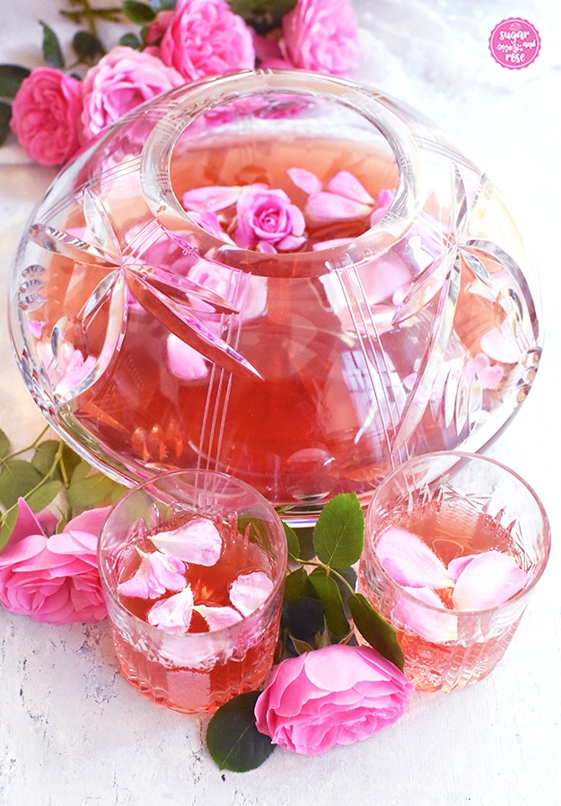 Rosenbowle in großem dickwandigen Bowleglasbehälter, davor zwei Bleikristallgläser mit Rosenbowle und Rosenblüten