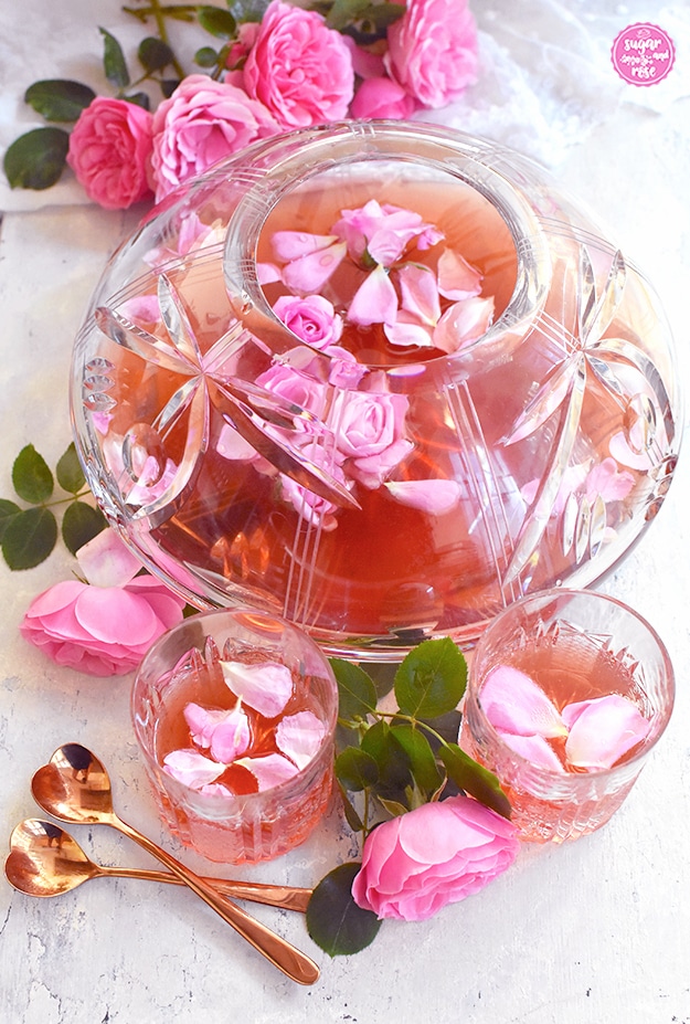Rosenbowle in großem Bleikristallglas mit rosa Petalen als Deko und rosa Blüten rund um die Bowle