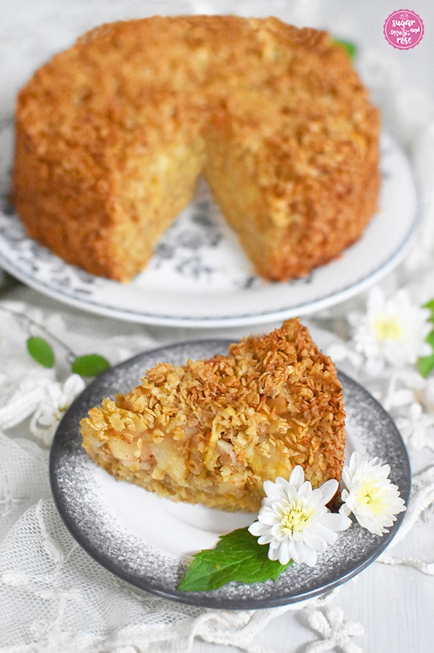 Apfelstreuselkuchen mit Haferflocken, ein Stück auf einem Teller, dekoriert mit weißen Crysanthemen