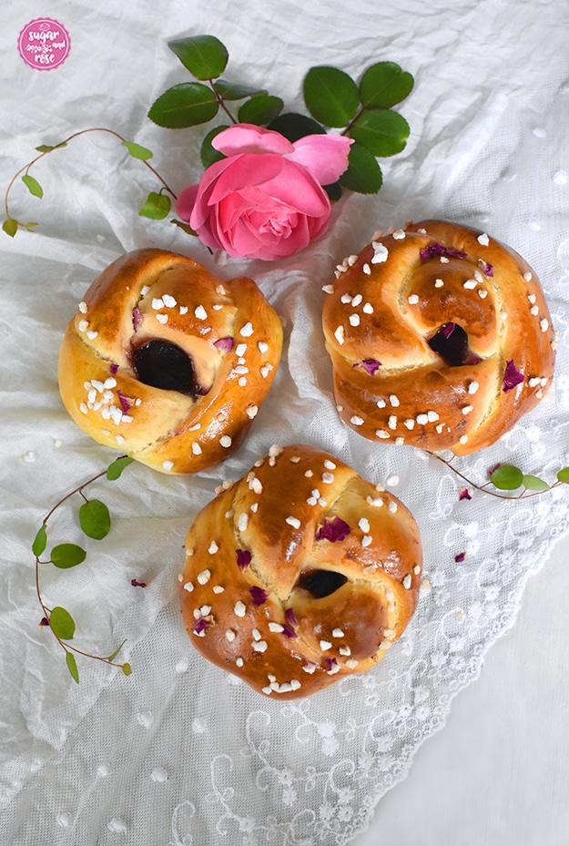 Drei fertig gebackene Rosen-Brioches mit Hagelzucker und getrockneten Rosenblüten