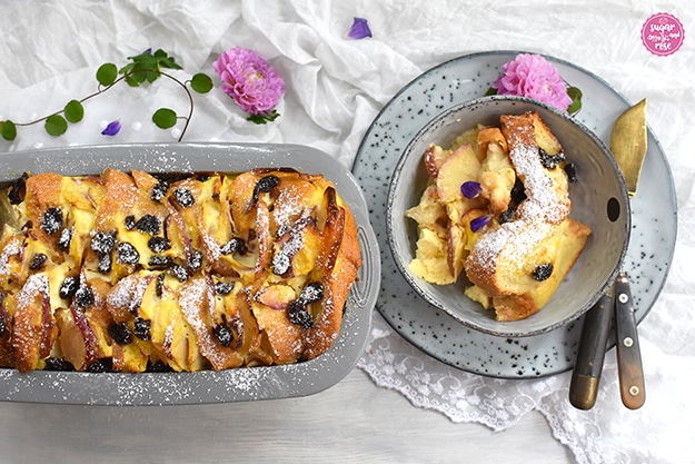 Scheichterhaufenportion auf Teller, dekoriert mit rosa Dahlien, lila Blüten und grünen Blättern auf weißem Spitzendeckchen