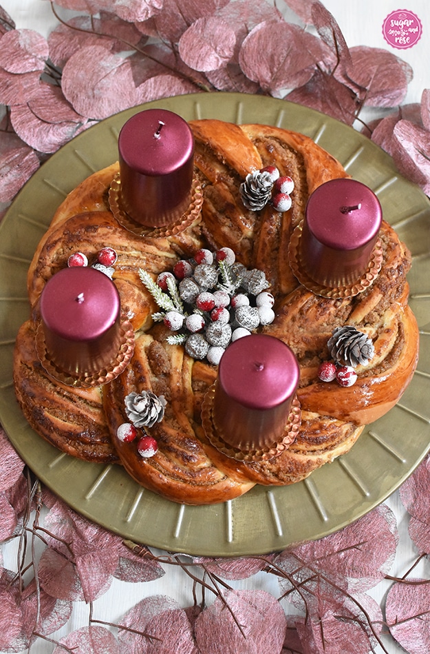 Hefe-Nusskranz auf Messingteller dekoriert wie ein Adventskranz mit vier weinroten Kerzen, kleinen mit Kunstschnee überzogenen Bockerl und rote Beeren