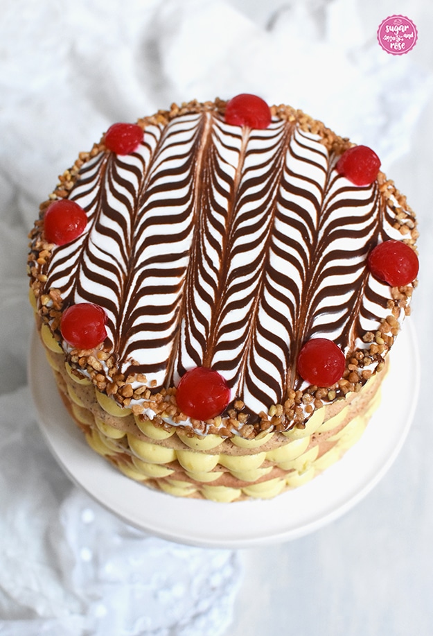 Esterházy-Torte von oben mit der typischen schwarz-weißen Esterhazy-Glasur, der oberste Boden rundum mit Krokant bestreut und mit kandierten roten Kirschen belegt